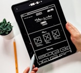 person holding black ipad with green plant